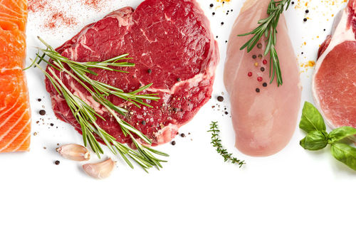 A salmon filet, a steak, a chicken breast, and a pork chop lain side by side covered in various spices and herbs